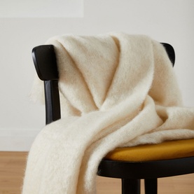 Foxford Off-White Mohair Throw draped over a black wooden chair, showing soft fluffy texture and fringe trim detail