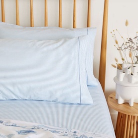 Foxford 300 Thread Count Blue Ticking Fitted Sheet with stripe print, styled on bed with matching pillowcases, beside wooden nightstand
