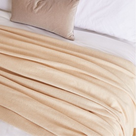 Foxford Extra Large Lambswool Throw in camel, draped over a bed, showing soft texture and generous size alongside a neutral cushion