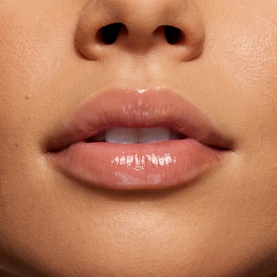 Model wearing Kylie Cosmetics Lip Butter lip balm, shown in a close-up shot with glossy, hydrated nude lips
