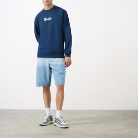 Model wearing Daily Paper Scratch Logo Sweatshirt in blue with crew neck, styled with light blue patterned shorts and grey trainers