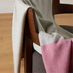 Foxford Lily Throw in grey and pink herringbone pattern, draped over a wooden chair, showing dual-sided design with fringe trim detail