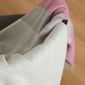 Foxford Lily Throw in multi, showing herringbone weave reverse, pink and grey checked face, with logo badge detail, draped over chair