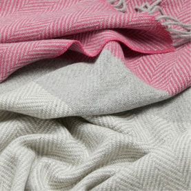 Foxford Lily Throw in pink and grey herringbone pattern, showing dual-sided design with soft lambswool texture and rolled fringe trim