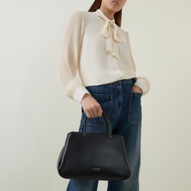 Model carrying Kate Spade Grace Satchel Crossbody Bag in black smooth leather with gold-tone hardware and top handles