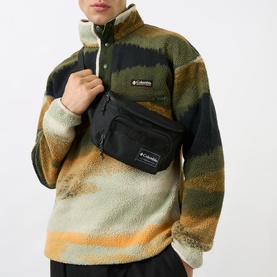 Model carrying Columbia Zigzag Bum Bag in black with logo print, worn crossbody, styled with a patterned fleece pullover