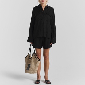 Model wearing Twist & Tango Melody Relaxed Fit Linen Shorts in black with matching black linen shirt, styled with sandals and a raffia tote bag