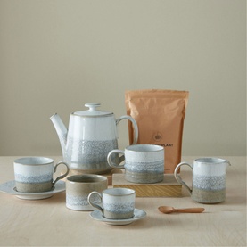 Denby Kiln Straight Teapot in beige stoneware, styled with matching mugs, cups, saucers, and a tea bag on a wooden tray