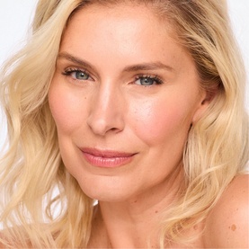 Model wearing Trinny London BFF De-Stress Tinted Serum in Claire, showing luminous, even complexion with natural, dewy skin finish