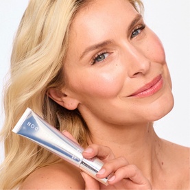 Model with Trinny London BFF De-Stress Tinted Serum in Claire, 30ml tube held near face, showing natural glowing complexion result