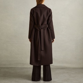 Model wearing Reiss Lucia Double-Breasted Coat in brown, rear view showing self-fabric waist belt and vent, styled with brown wide-leg trousers
