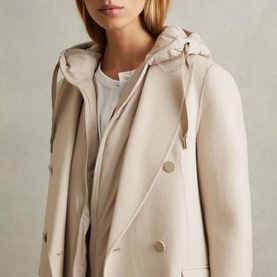 Model wearing Reiss Maeve Double-Breasted Trench Coat in beige wool-blend, styled with a detachable hood and white top underneath