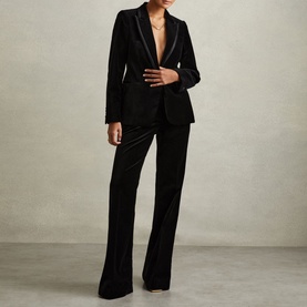 Model wearing Reiss Parisa Single-Breasted Velvet Blazer in black with satin peak lapels, styled with matching black velvet wide-leg trousers