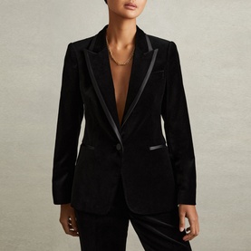 Model wearing Reiss Parisa Single-Breasted Velvet Blazer in black with satin lapels, styled with matching black velvet trousers