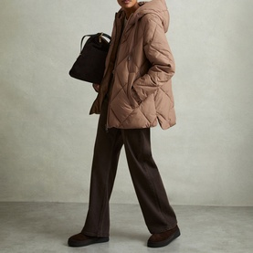 Model wearing Reiss Thea Diamond Quilted Coat in beige with brown wide-leg trousers, carrying a black bucket bag
