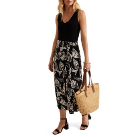 Model wearing Phase Eight Ayana Printed Skirt in black leaf print midi length, styled with black vest top and sandals, carrying woven tote bag