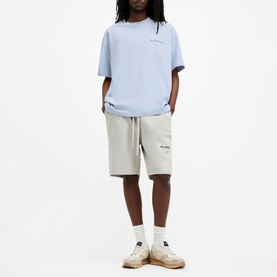 Model wearing All Saints Access Logo Oversized T-Shirt in blue, styled with light grey drawstring shorts and cream trainers