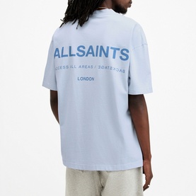 Model wearing All Saints Access Logo Oversized T-Shirt in blue, back view showing ALLSAINTS London graphic print, paired with light grey trousers