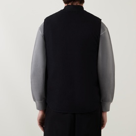 Model wearing Carhartt Logo Vest Gilet in black, back view, sleeveless with rib-knit collar, styled with grey long-sleeve top
