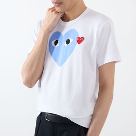 Model wearing Comme Des Gar&ccedil;ons Play Double-Heart Logo T-Shirt in white with blue and red heart graphic. Styled with dark trousers.