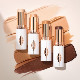 Four Charlotte Tilbury foundation sticks in a range of shades from fair to deep, with gold caps and white packaging, shown with shade swatches.