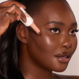 Model with a rose gold facial roller or highlighting tool applied to cheekbone, glowing skin finish visible