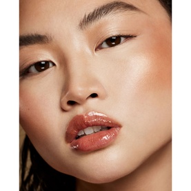 Model wearing FENTY Gloss Bomb Oil in Fro$ted Bunz, a warm terracotta gloss, paired with a sun-kissed, glowy complexion look