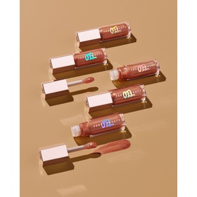 Fenty Gloss Bomb Oil in Fro$ted Bunz, set of four 9ml lip gloss tubes with gold caps arranged on warm beige background