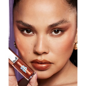 Model with FENTY Gloss Bomb Oil in Coppa Cookie, a warm copper-brown lip gloss oil, held up close to glossy lips. 9ml