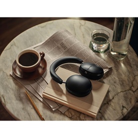 Sonos Ace Headphones in black, resting on books on a marble table alongside a coffee cup and glass