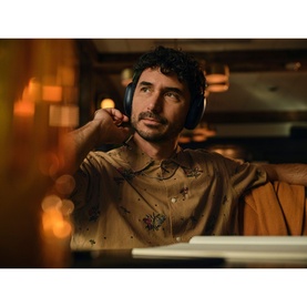 Model with Sonos Ace Headphones in black, worn over ears, seated in a warmly lit ambient setting