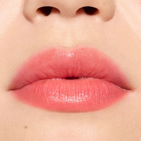 Close-up of lips wearing MAC Glow Play Tendertalk Lip Balm in a sheer coral-pink shade with a glossy finish