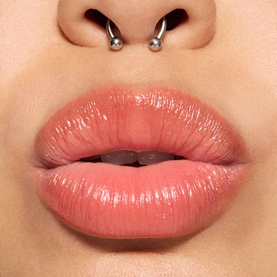 Model wearing MAC Glow Play Tendertalk Lip Balm in a sheer rosy nude gloss finish, shown in a close-up lip shot
