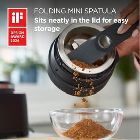 Kenwood Autograph Duo Prep 2 in 1 Chopper/Grinder in black, folding mini spatula sits in lid, grinding spices into glass bowl.
