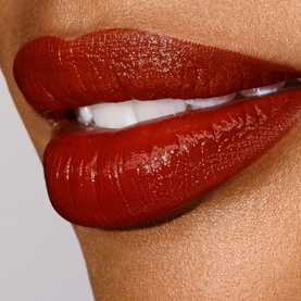 Est&eacute;e Lauder Pure Colour Explicit Slick Shine Lipstick in deep brick-red shade applied to model's lips, showing glossy high-shine finish