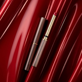Est&eacute;e Lauder Pure Colour Explicit Slick Shine Lipstick 2.8g with gold-toned cap, shown open on red satin background