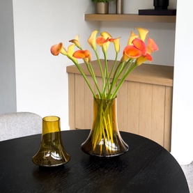 XL Boom Spinn Vase Large in brown glass, styled on a dark table with orange calla lilies, alongside the smaller Spinn Vase