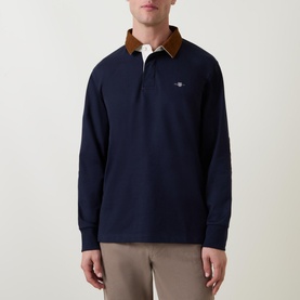Model wearing Gant Corduroy Collared Rugby Shirt in navy with brown corduroy collar, long sleeves, and logo embroidery, styled with beige trousers