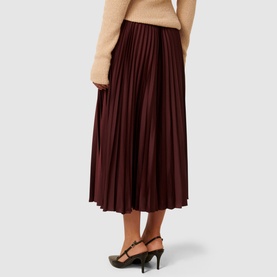 Model wearing Forever New Estelle High-Rise Pleated Skirt in deep burgundy satin, styled with a beige knit top and black heels