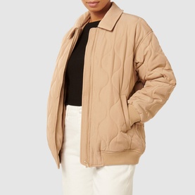 Model wearing Forever New Jacinta Quilted Jacket in brown, featuring classic collar, front zip fastening and welt pockets, styled with white trousers