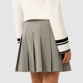 Model wearing Forever New Montana Pleated Mini Skirt in grey check with pleated detailing, styled with a white varsity-cuff jumper