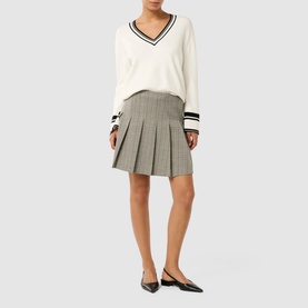 Model wearing Forever New Montana Pleated Mini Skirt in grey check with pleated detailing, styled with a white V-neck jumper and black flats