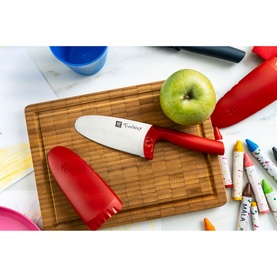 Zwilling Twinny Kids Chef Knife in red with rounded blade and red finger guard on wooden chopping board beside a green apple