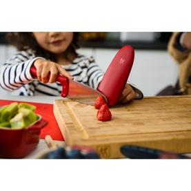 Child using Zwilling Twinny Kids Chef Knife Red to slice strawberries on wooden board, showing finger guard safety feature