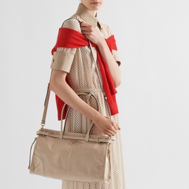 Model carrying Prada Accessories Bonnie Large Leather Handbag in cream with gold-tone hardware and buckle strap detailing