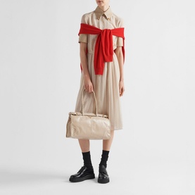 Model carrying Prada Accessories Bonnie Large Leather Handbag in cream with gold-tone hardware, styled with a beige shirtdress and red knitwear