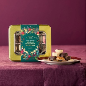Cartwright & Butler Merry Christmas Belgian Chocolates Selection in festive gold tin, with assorted chocolates displayed on a plate beside it