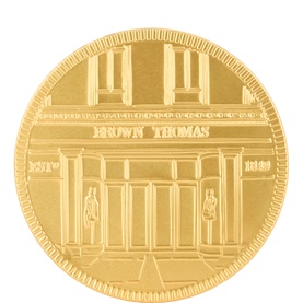 Brown Thomas gold-tone commemorative coin medallion featuring engraved storefront facade design with milled edge detail