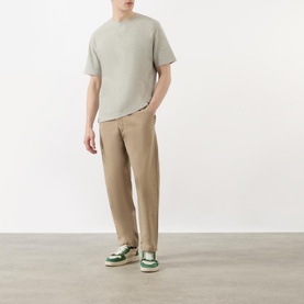 Model wearing Wax London Kurt Drawstring Casual Trousers in khaki, styled with a sage green tee and green and white trainers
