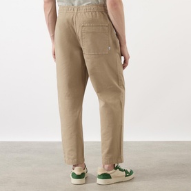 Model wearing Wax London Kurt Drawstring Casual Trousers in khaki, back view showing patch pocket, styled with green and white trainers